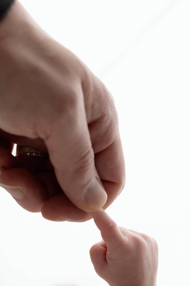 A newborn gripping a parent's finger against a white background.