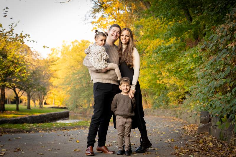 Family of four photographed on a park path under autumn trees.