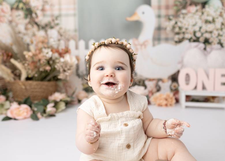 Grinning one year old covered in frosting at a floral first birthday setup.